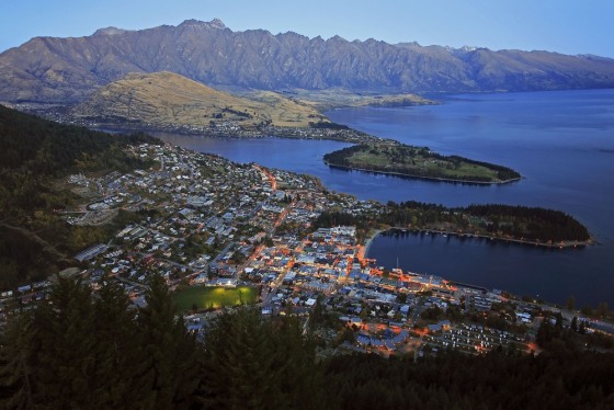 The twinkling lights of Queenstown, New Zealand, seen from the air, with the Kelvin Peninsula and Lake Wakatipu in the distance.